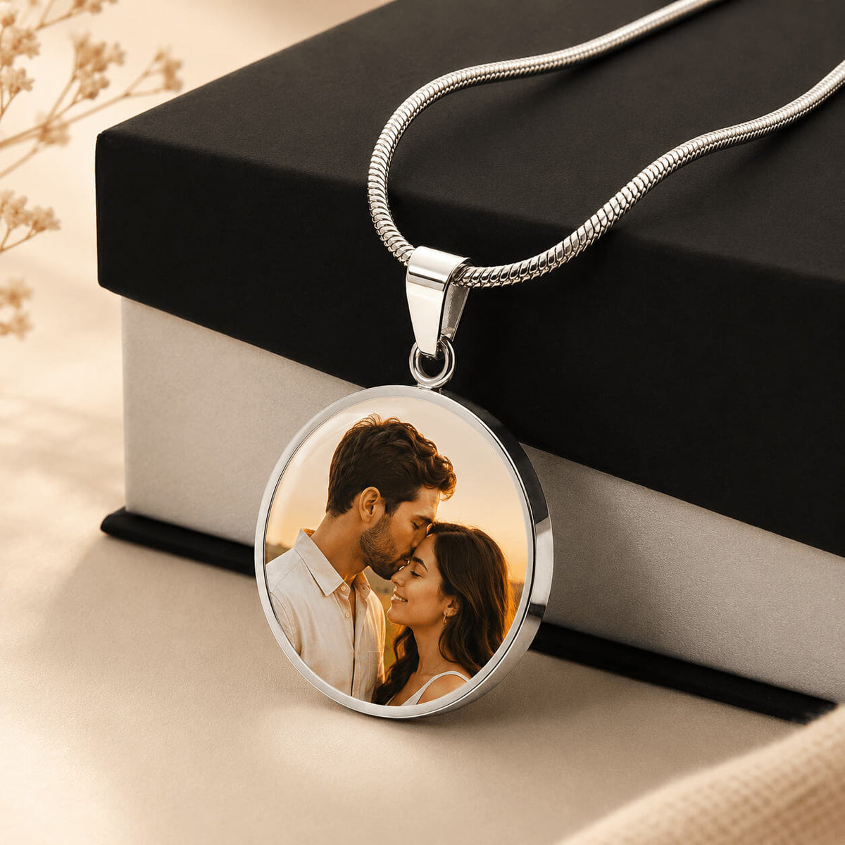 Silver personalized circle photo necklace with couple portrait displayed beside gift box